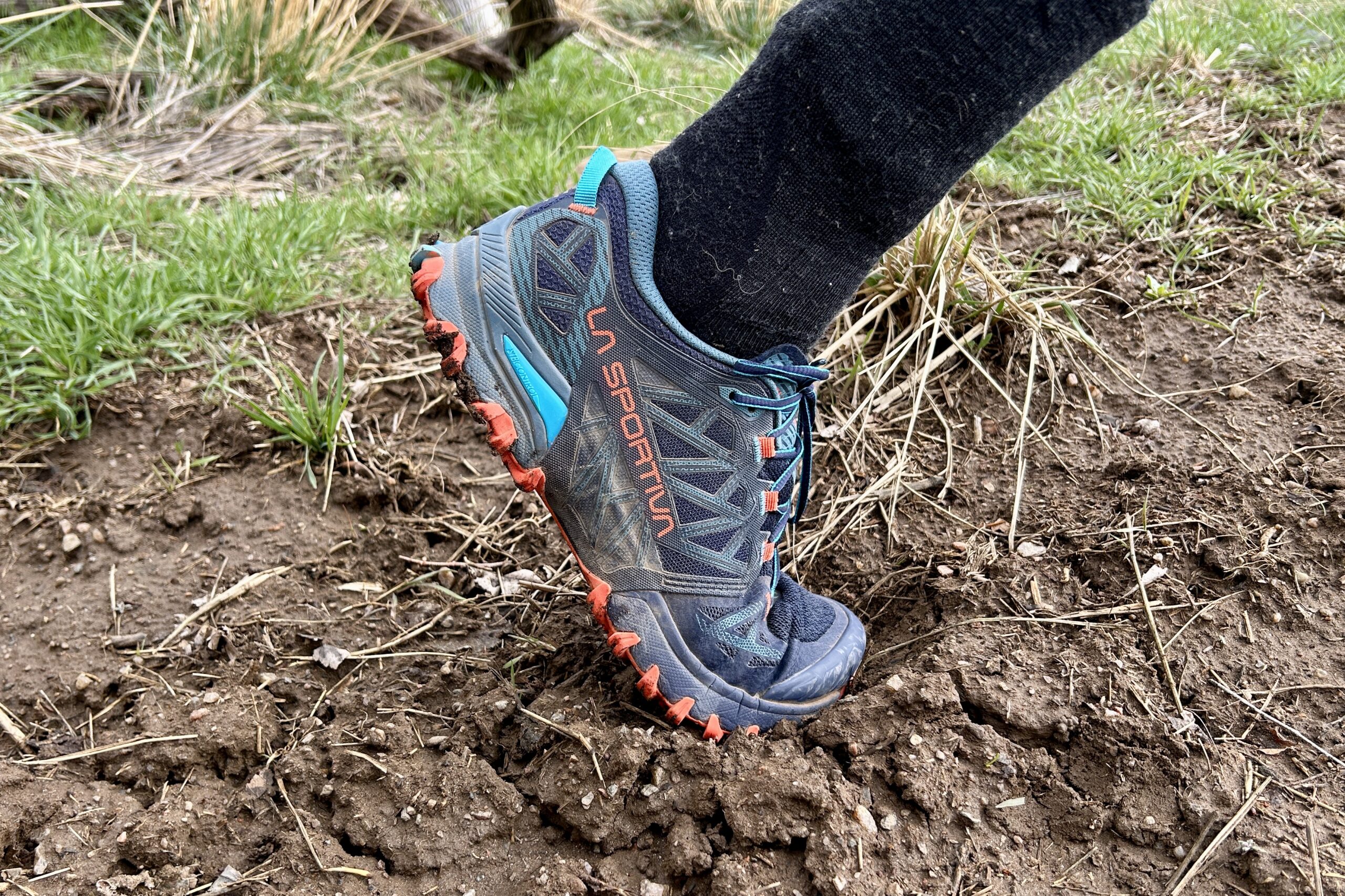 Close up side view of a person wearing a trail runner through thick mud.
