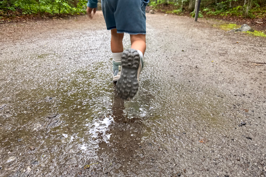 Close-up of child running through a puddle on a forest trail wearing Adidas Terrex AX4R Mid shoes.
