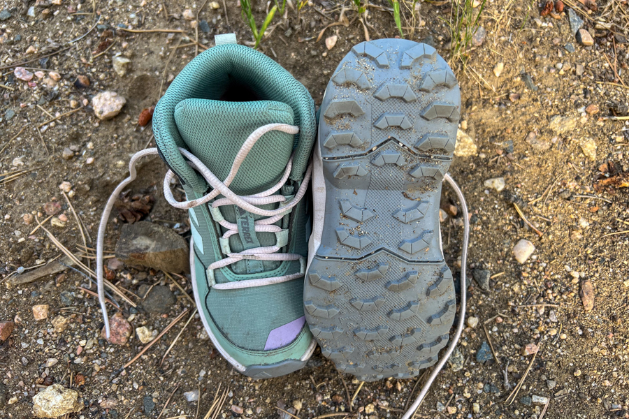 Close-up of Adidas Terrex AX4R Mid kids’ hiking shoes showing tread pattern and high ankle collar on rocky dirt ground.