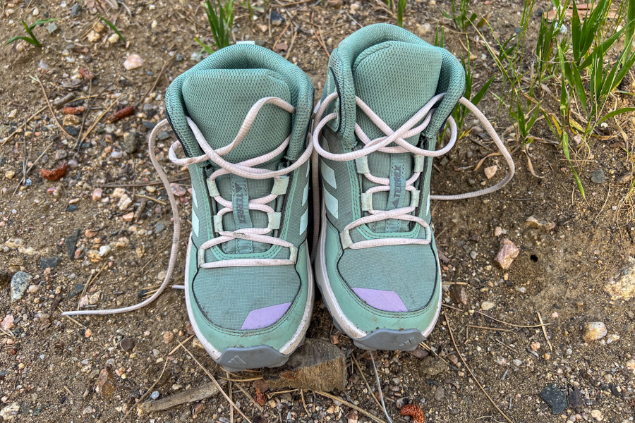 Front view of a pair of Adidas Terrex AX4R Mid hiking shoes for kids sitting on dirt with visible laces and toe protection.