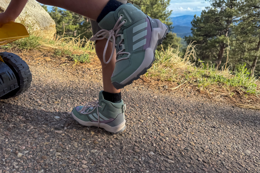 Child lifting one foot while standing on a slope wearing Adidas Terrex AX4R Mid shoes.