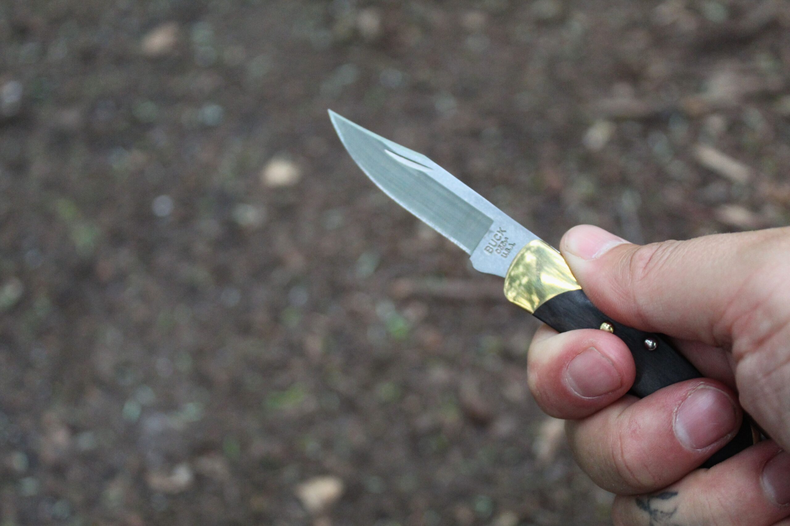 Holding an open Buck Knives 055 Pocket Knife with a dirt background