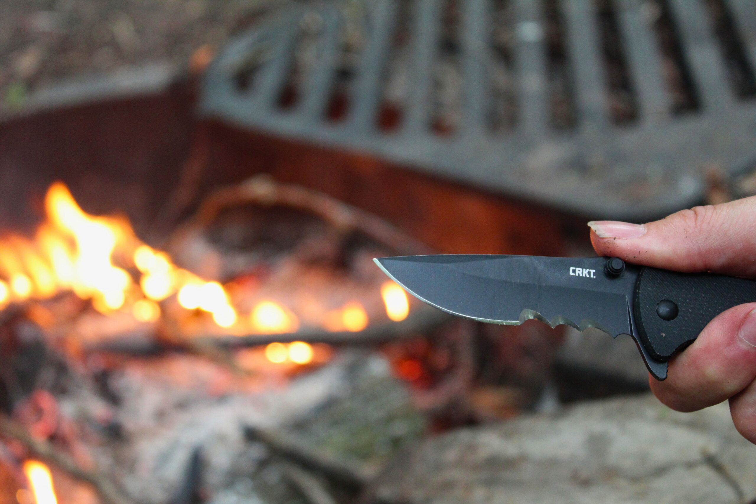 The CRKT Drifter Pocket Knife open showing close up of the blade with a fire in the background