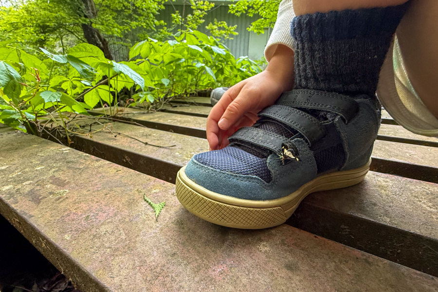 Close-up of a child wearing Five Ten Freerider kids’ bike shoes with Velcro straps while sitting on a metal bridge.