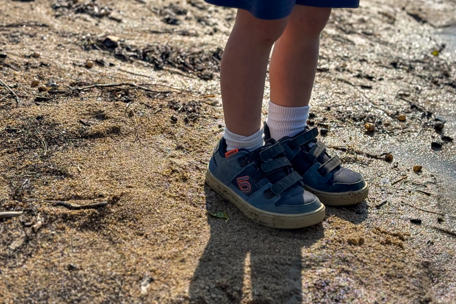 Child wearing Five Ten Freerider shoes standing in wet sand near water.