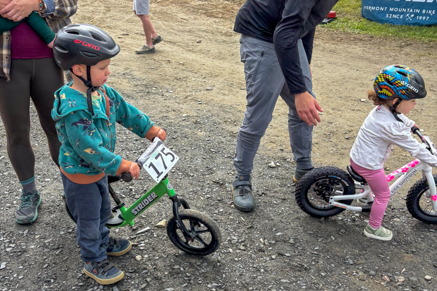 Two young children on balance bikes wearing helmets, one of them wearing Five Ten Freerider shoes at a bike park event.