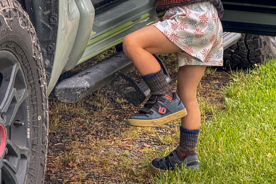 Child wearing Five Ten Freerider shoes stepping into a truck with muddy tires.
