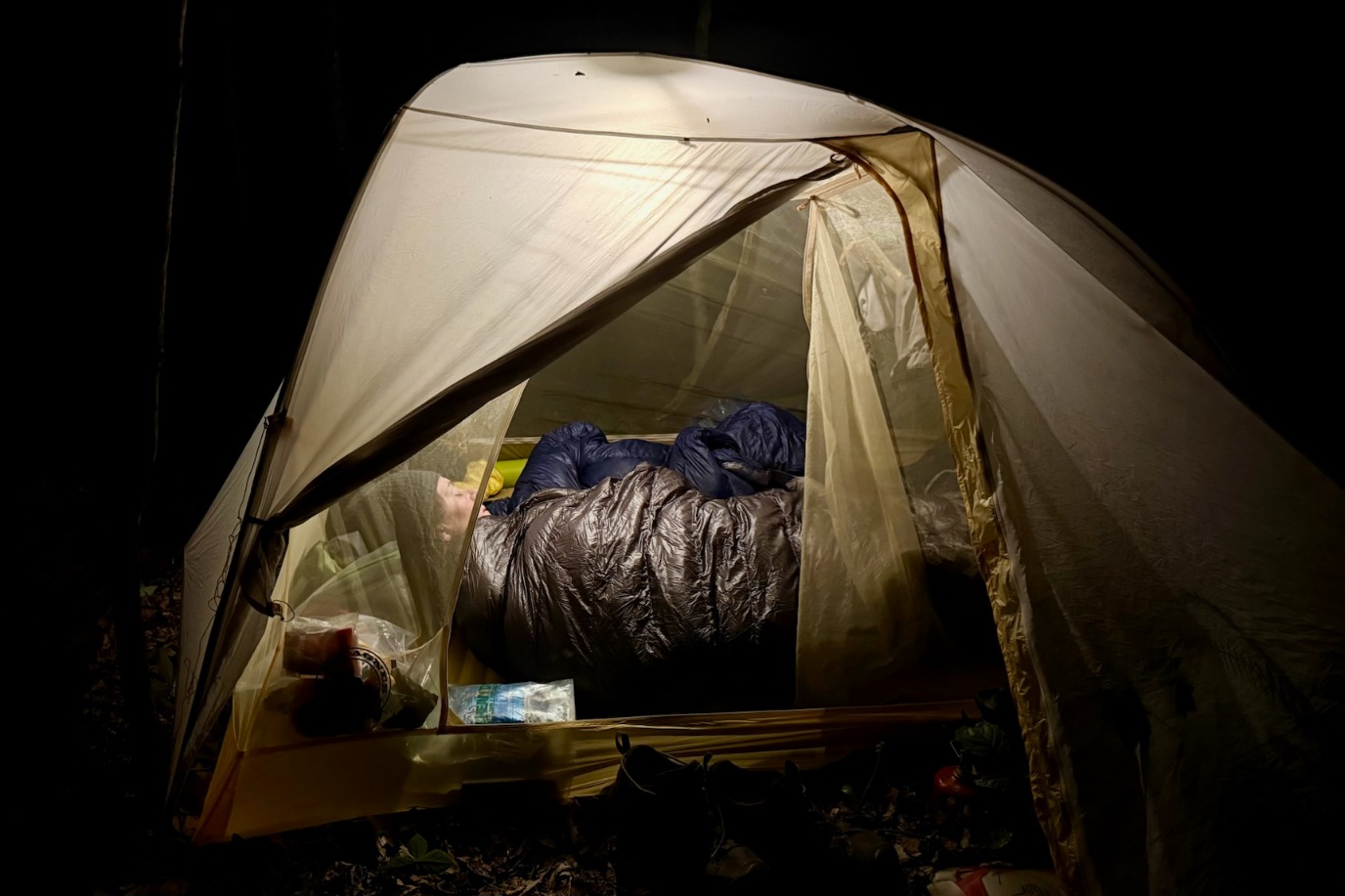 Hiker sleeping in a Western Mountaineering AstraLite Quilt in a tent at night