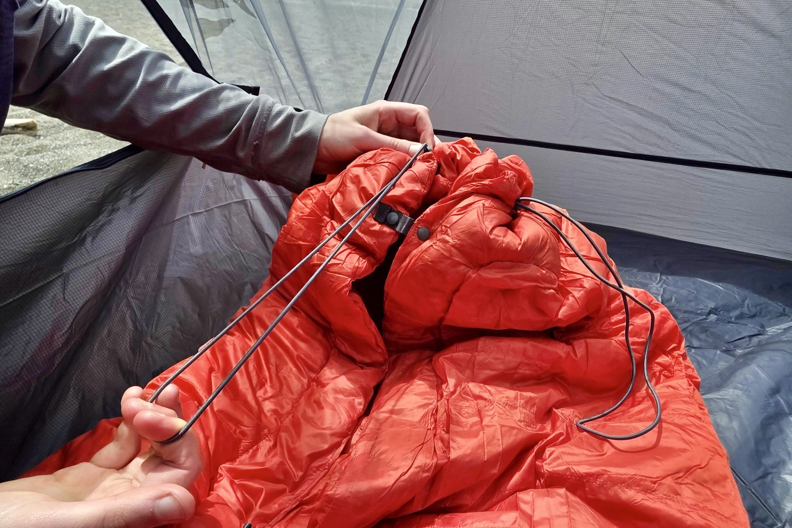 A woman cinches down the foot box of her minimalist sleeping bag.