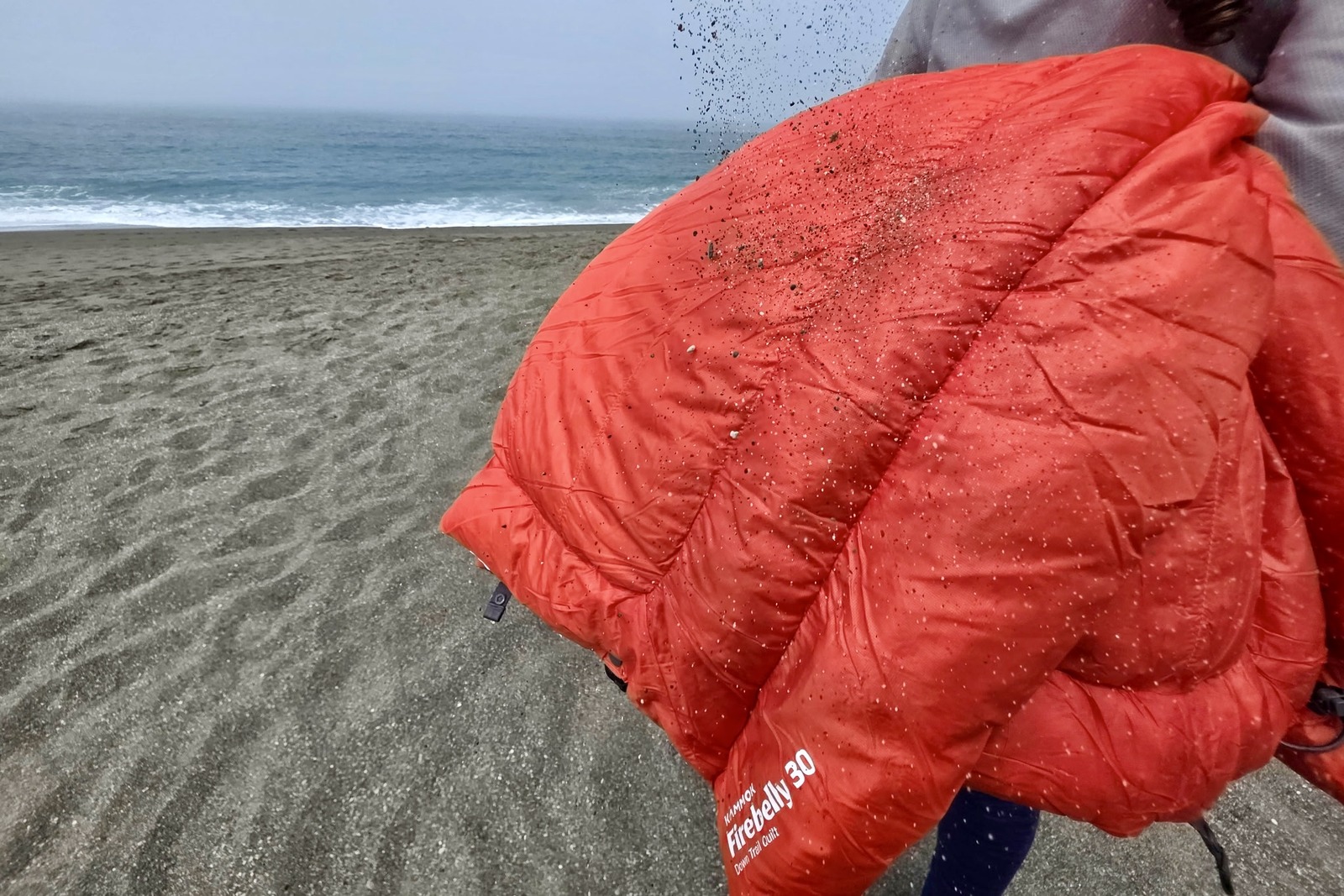 A woman shakes sand off her blanket at the beach.