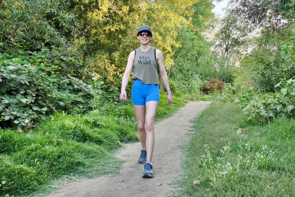 A woman walks along a lush trail surrounded by greenery.