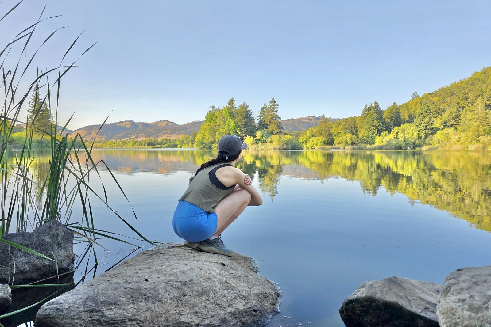 A woman squats on a rock in front of a lake