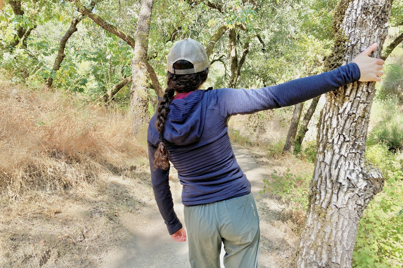 A woman braces her hand against a tree as she looks at the trail ahead.