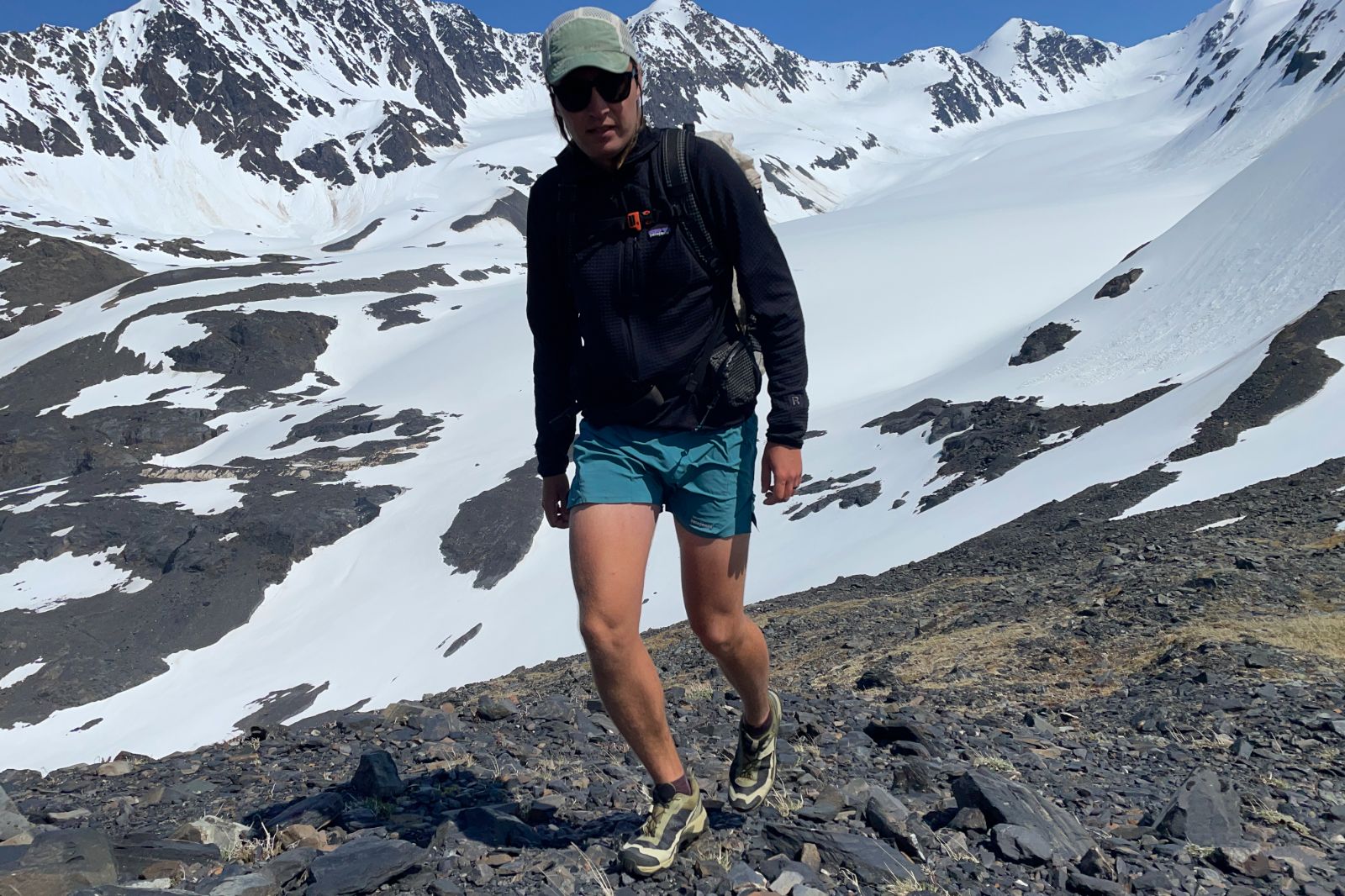 A man hikes along an alpine pass above a glacier.
