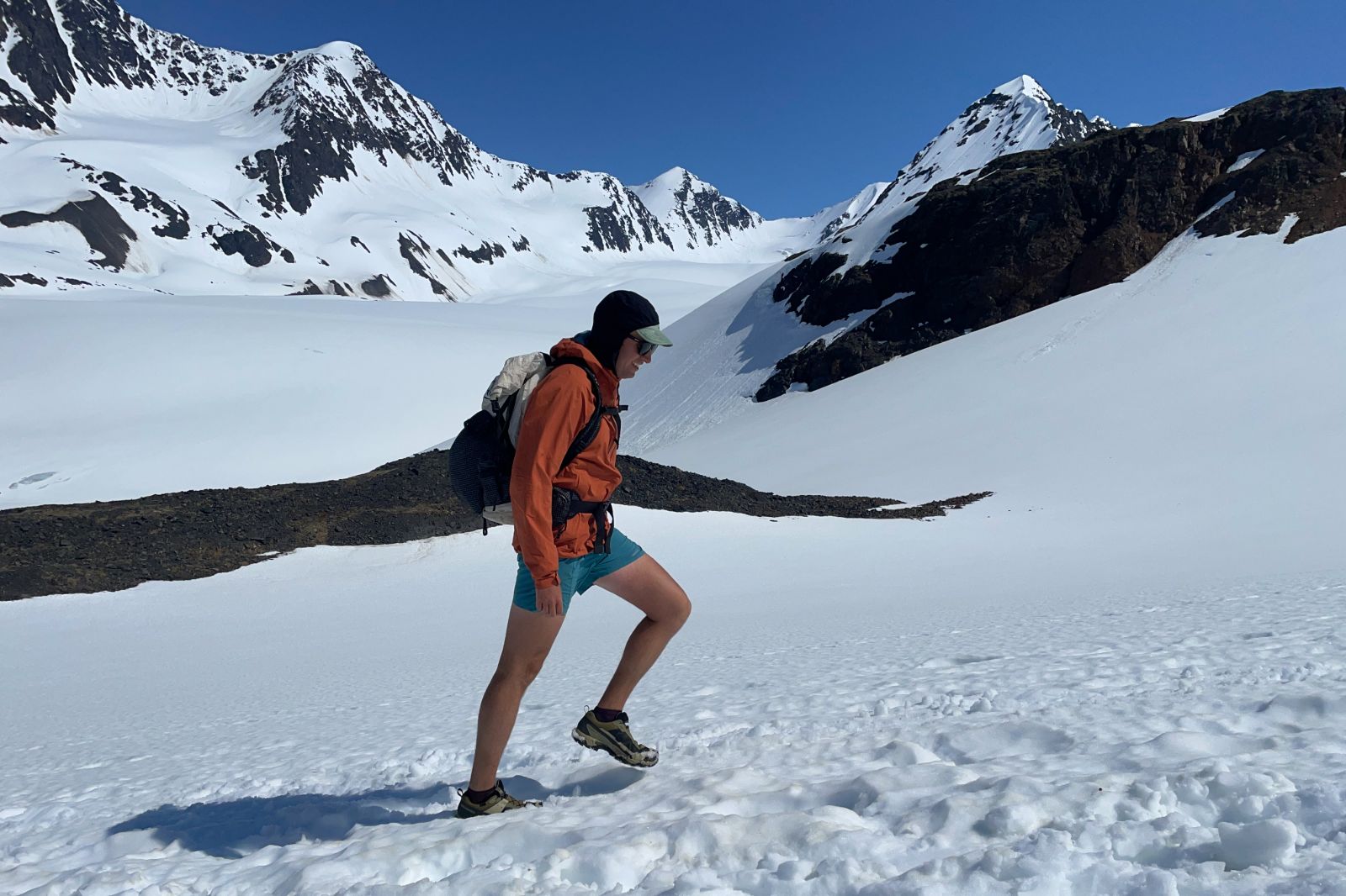 A man hikes across a snowy mountain pass.