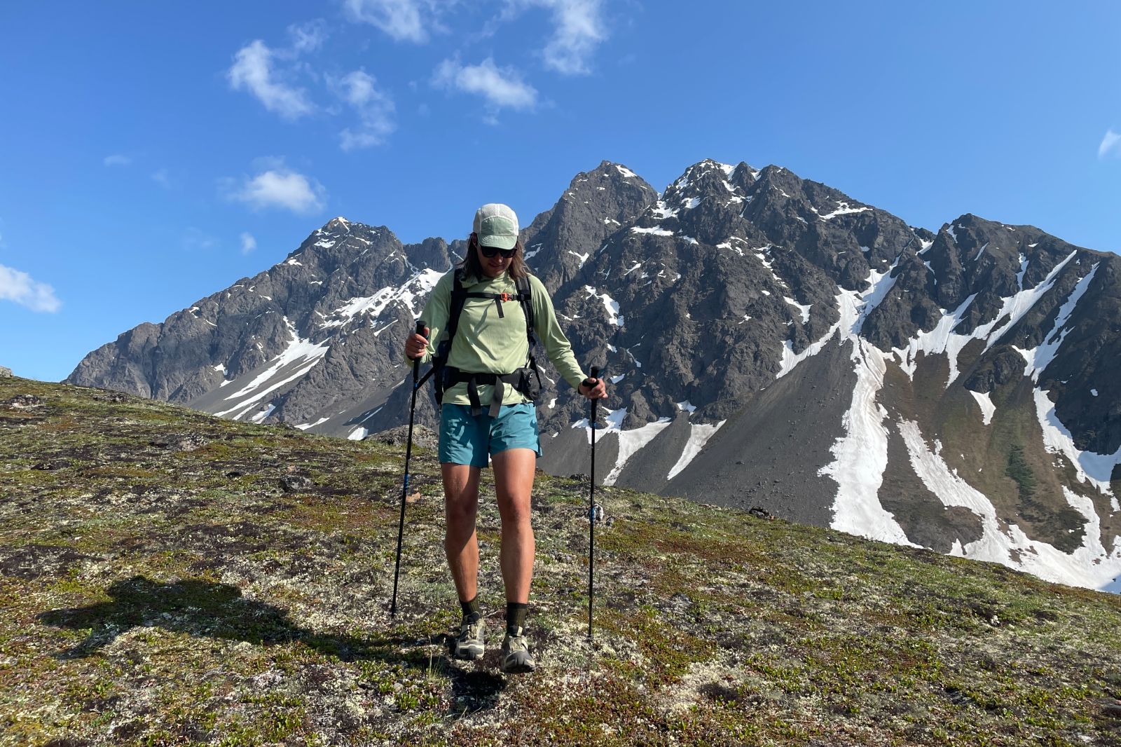 A man hikes with craggy mountains in the background.