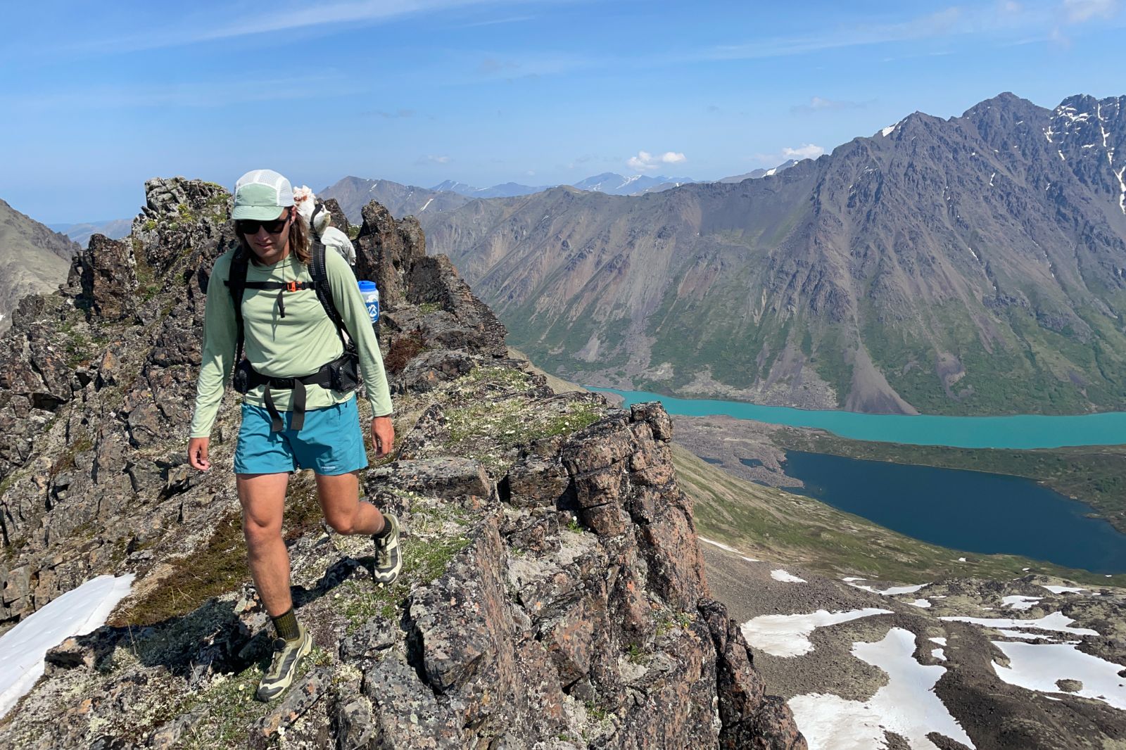 A man hikes along an alpine ridgeline above lakes.