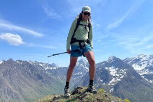 A man stands on a summit with mountain vistas.