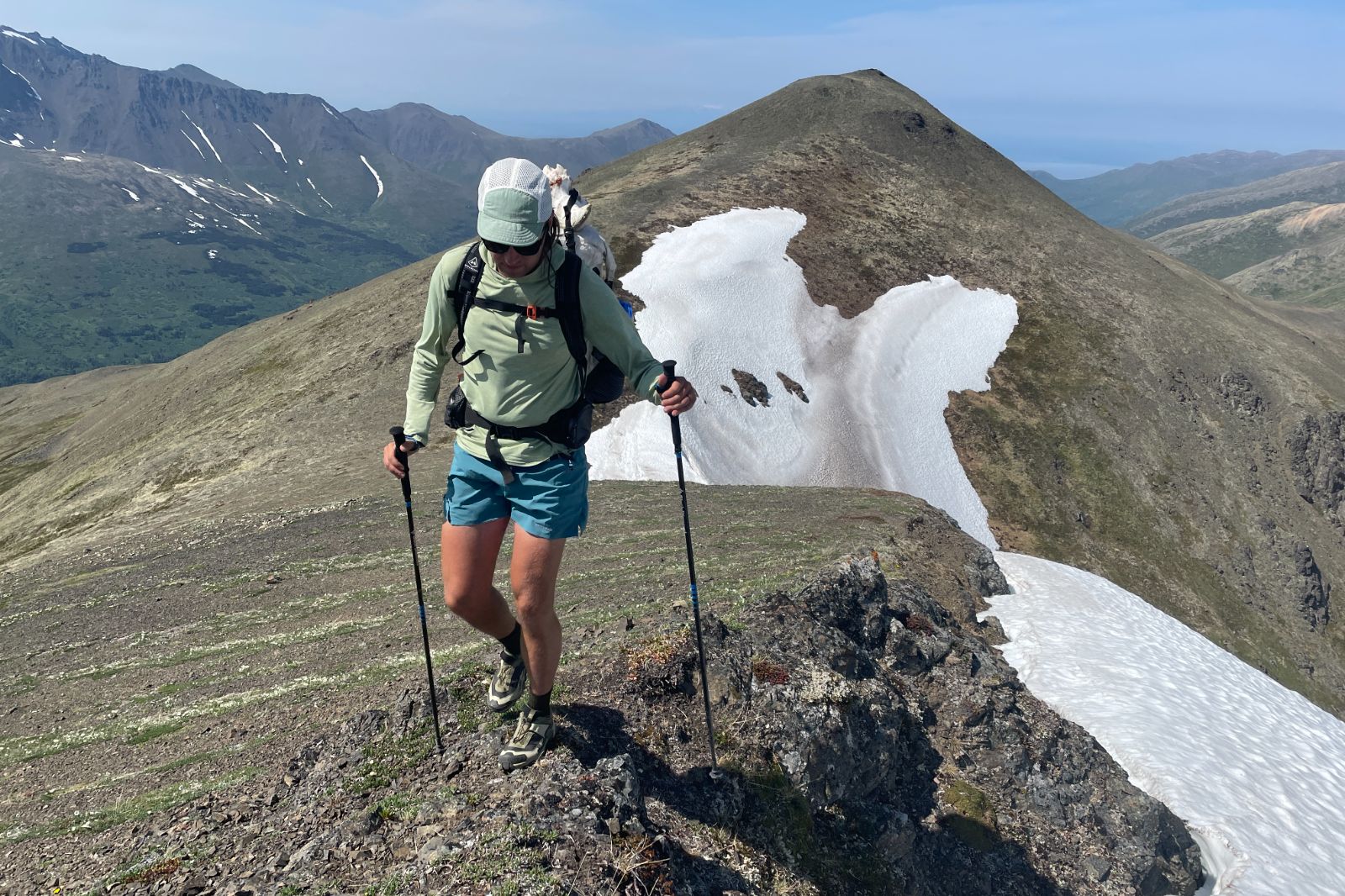 A man walks along a ridgeline in blue shorts.