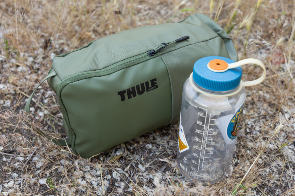 The Thule Chasm 40L duffel shown packed up into the included pouch next to a 32oz Nalgene. The Nalgene is perhaps 2 inches thinner and shorter than packed duffel.