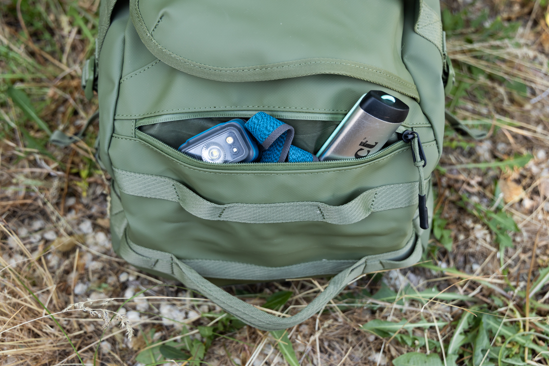 Small items like a cathole shovel and headlamp peak out of the exterior zipper pocket on the end of the Thule Chasm duffel.