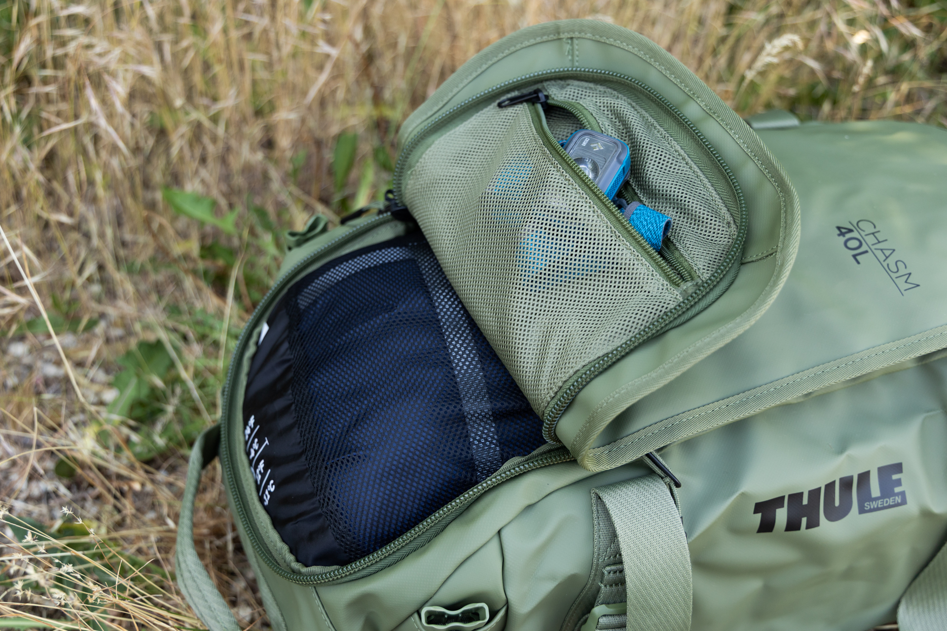 The unique U-shaped lid on one end of the Thule Chasm duffel shown open. Yo can see that it provides easy access to a small accessory pocket inside the lid that is flipped open when the rest of the lid is zipped shut.