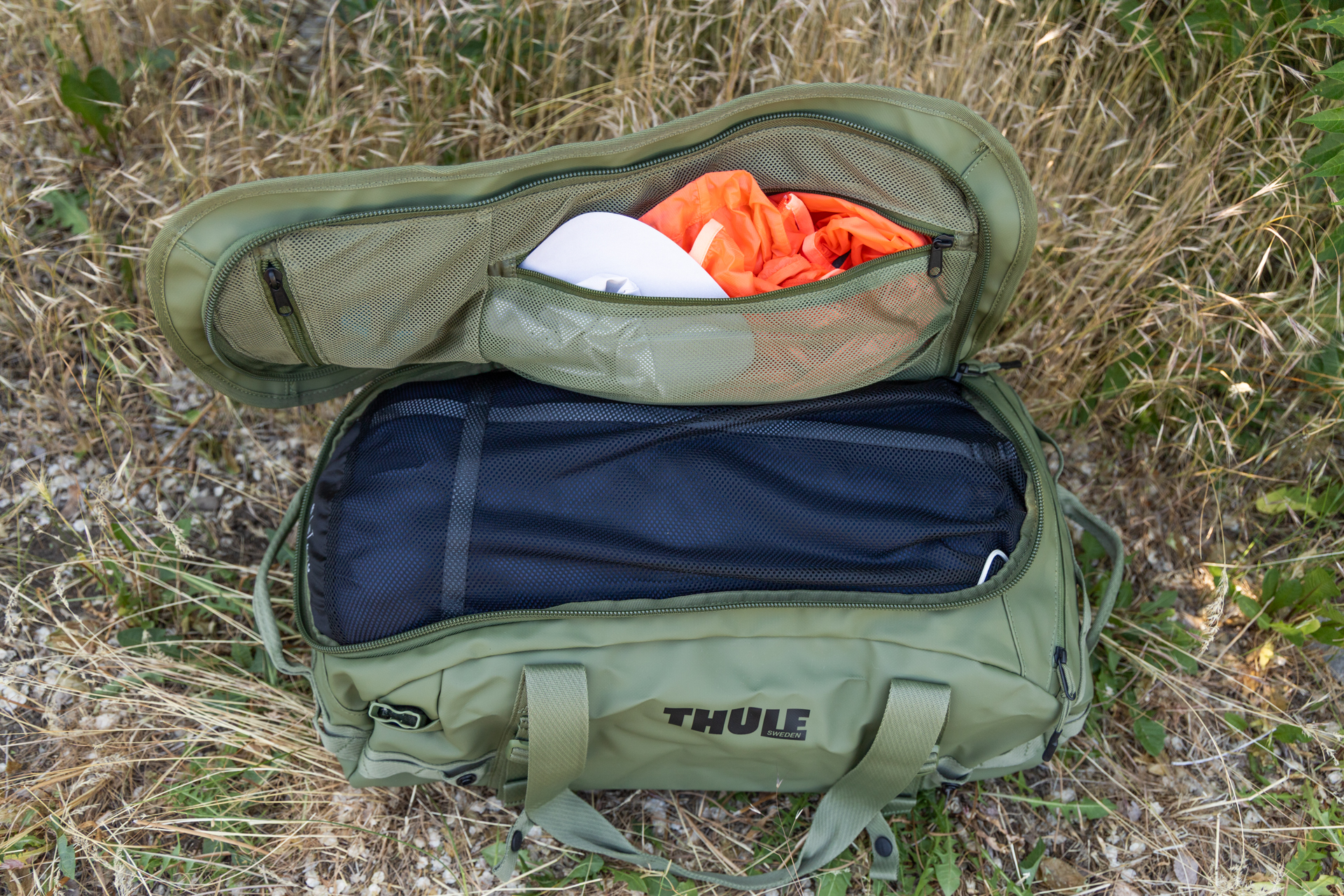 A top-down view of the Thule Chasm 40L duffel fully unzipped and open with a sleeping bag packed inside and a cap and jacket visible through the one of two open zippered accessory pockets in the lid.