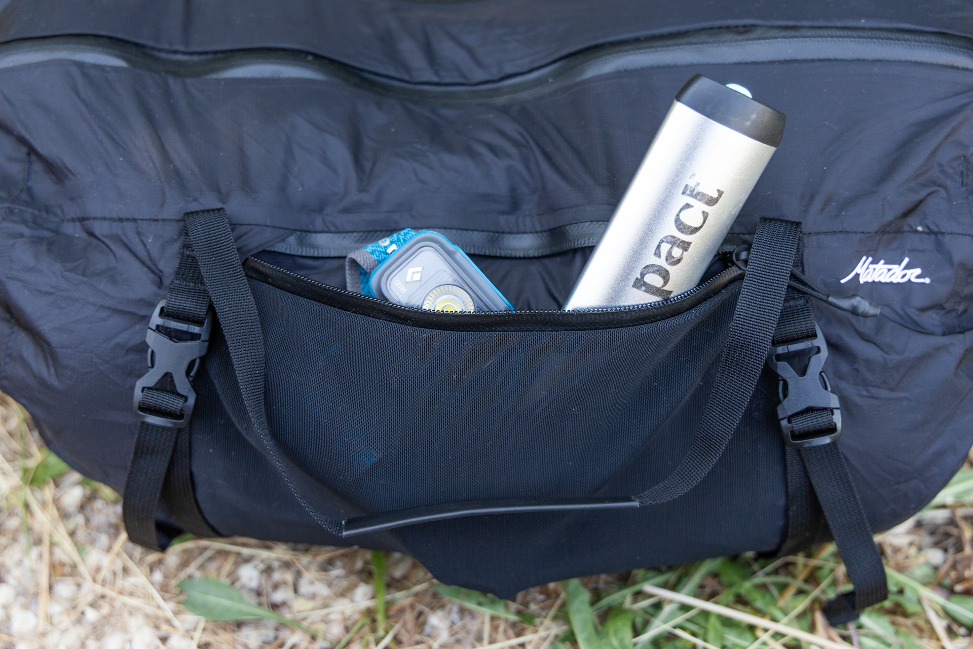 A spade and a headlamp peak out of the open stretch mesh zipper pocket on one side of the Matador Freefly Packable Duffel.