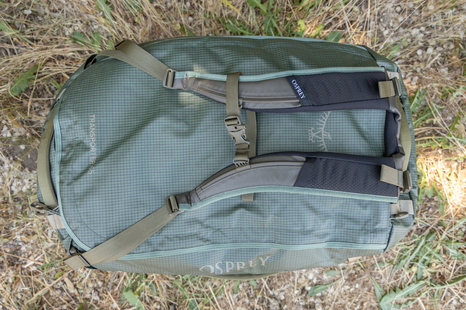 A top-down look at the Osprey Transporter duffel with backpack straps deployed. A sternum strap is bucked between them.
