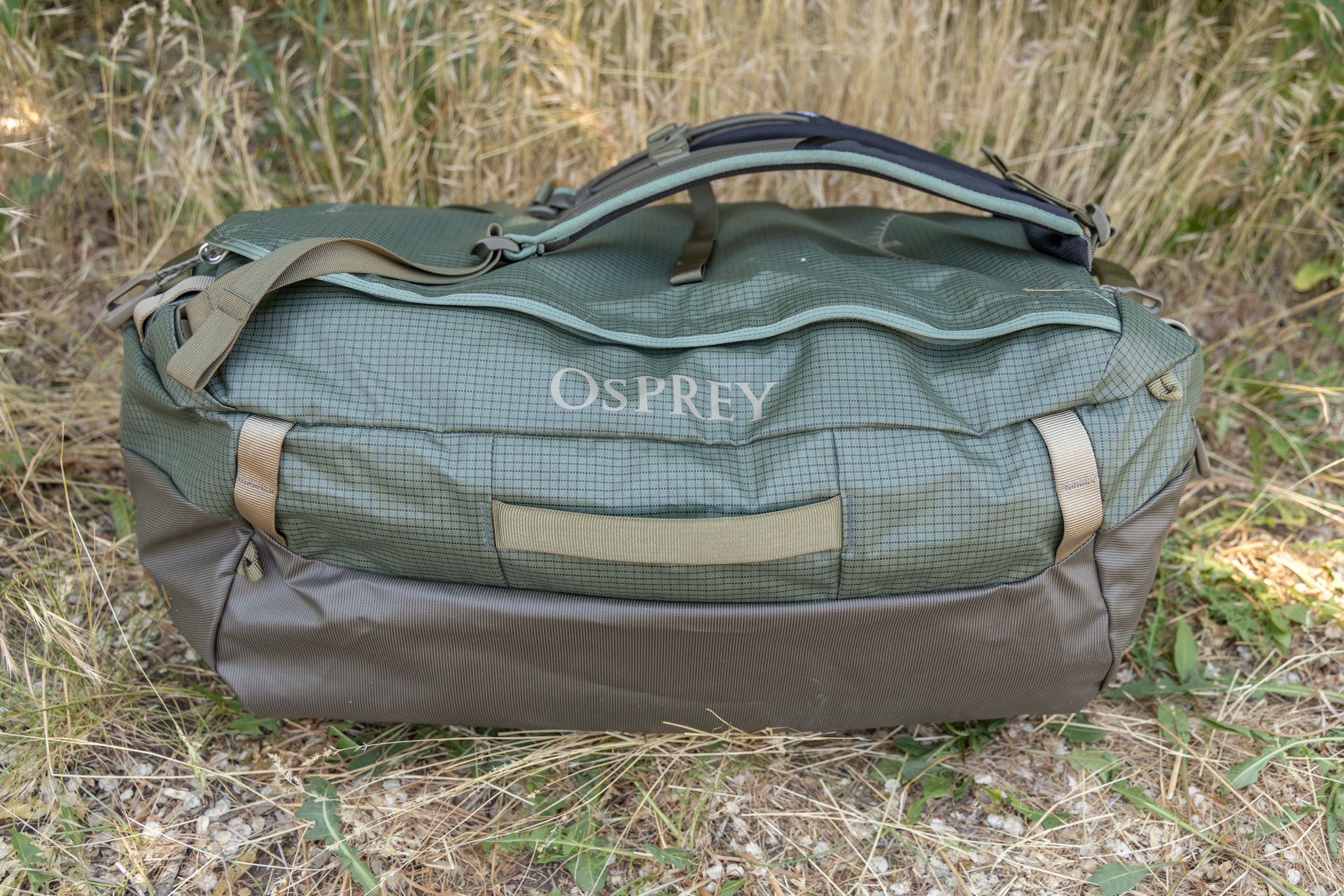 A side view of the Osprey Transporter duffel shows durable materials, heavy duty cargo handles on the side, webbing loops, and backpack straps attached atop the lid.