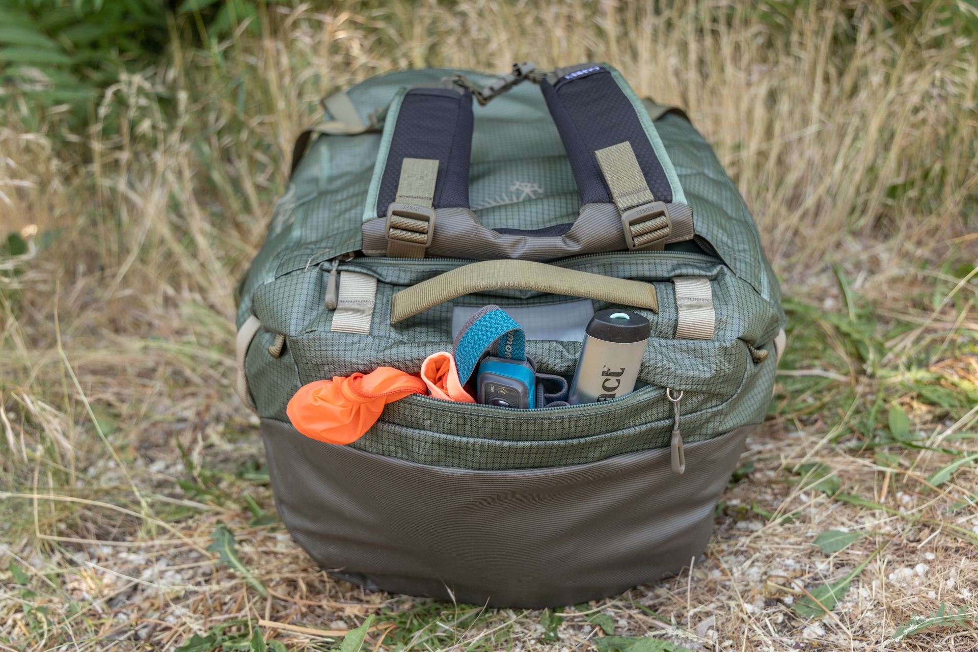 One end of the Osprey Transporter duffel with an exterior accessory pocket. A rain jacket, spade and headlamp peek out of the open zipper.