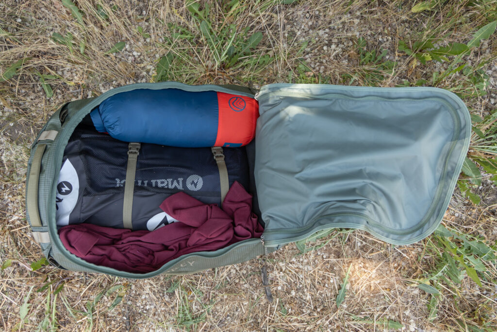 A top-down view of the open Osprey Transporter duffel. The lid opens clamshell style, hinging on a short end, and the interior is full of gear like jackets and sleeping bags.