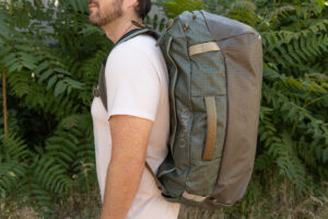A side view of a man carrying the Osprey Transporter duffel as a backpack. It hugs his back closely.