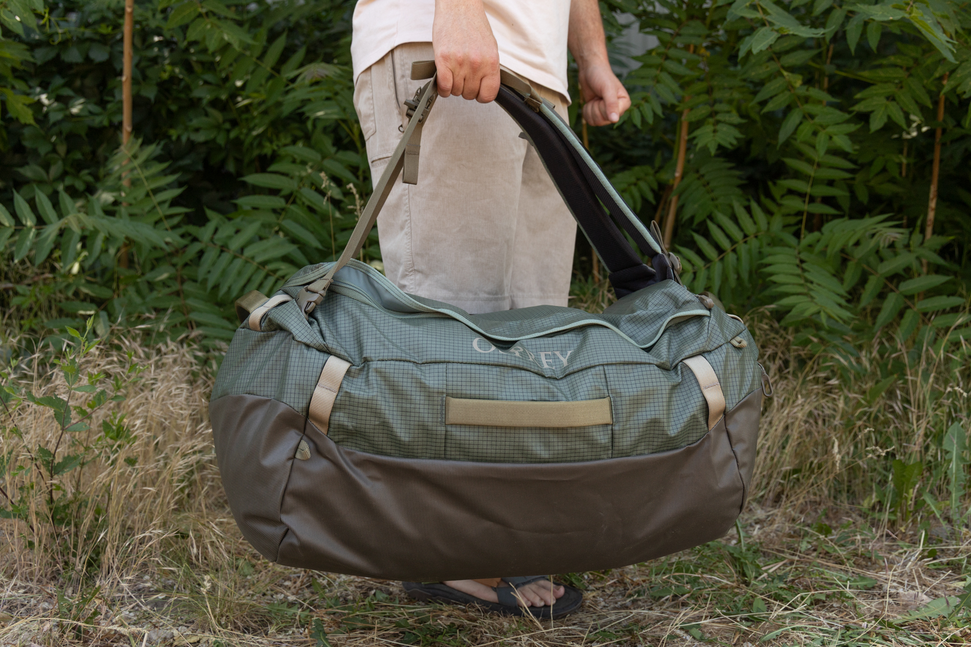 A side view of a man carrying the Osprey Transporter duffel using the backpack straps as grab handles. The straps aren't designed to fit in his hands easily.