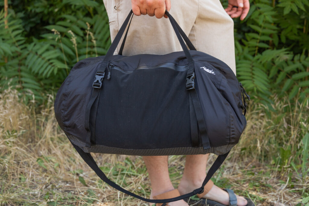 A man carries the Matador Freefly Packable Duffel at his side using the top duffel handles. The shoulder strap dangles underneath.