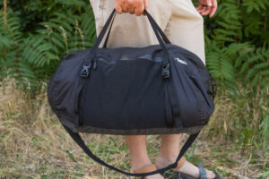 A man carries the Matador Freefly Packable Duffel at his side using the top duffel handles. The shoulder strap dangles underneath.