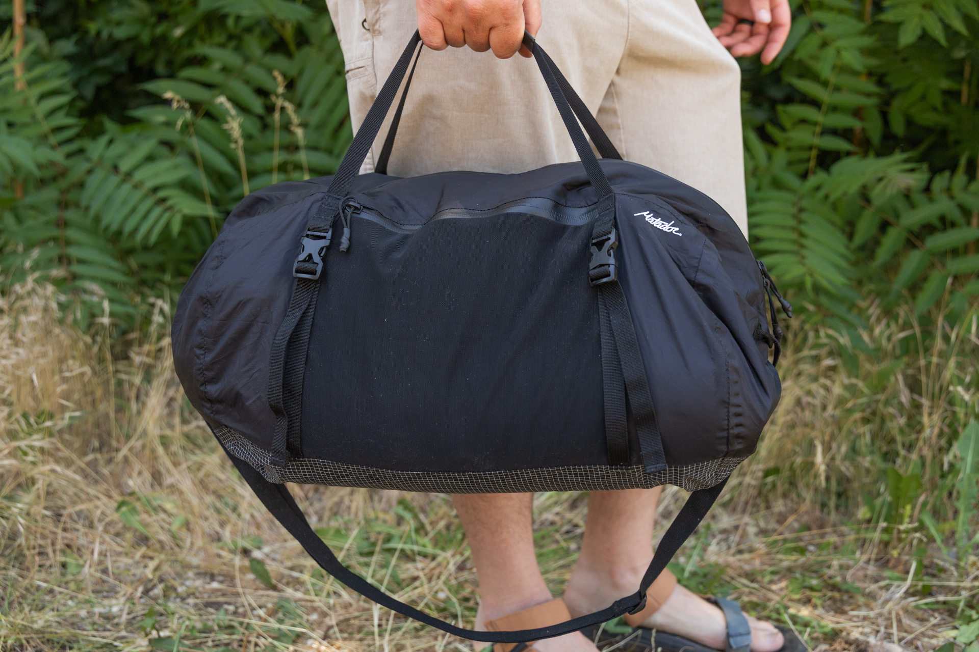 A man carries the Matador Freefly Packable Duffel at his side using the top duffel handles. The shoulder strap dangles underneath.