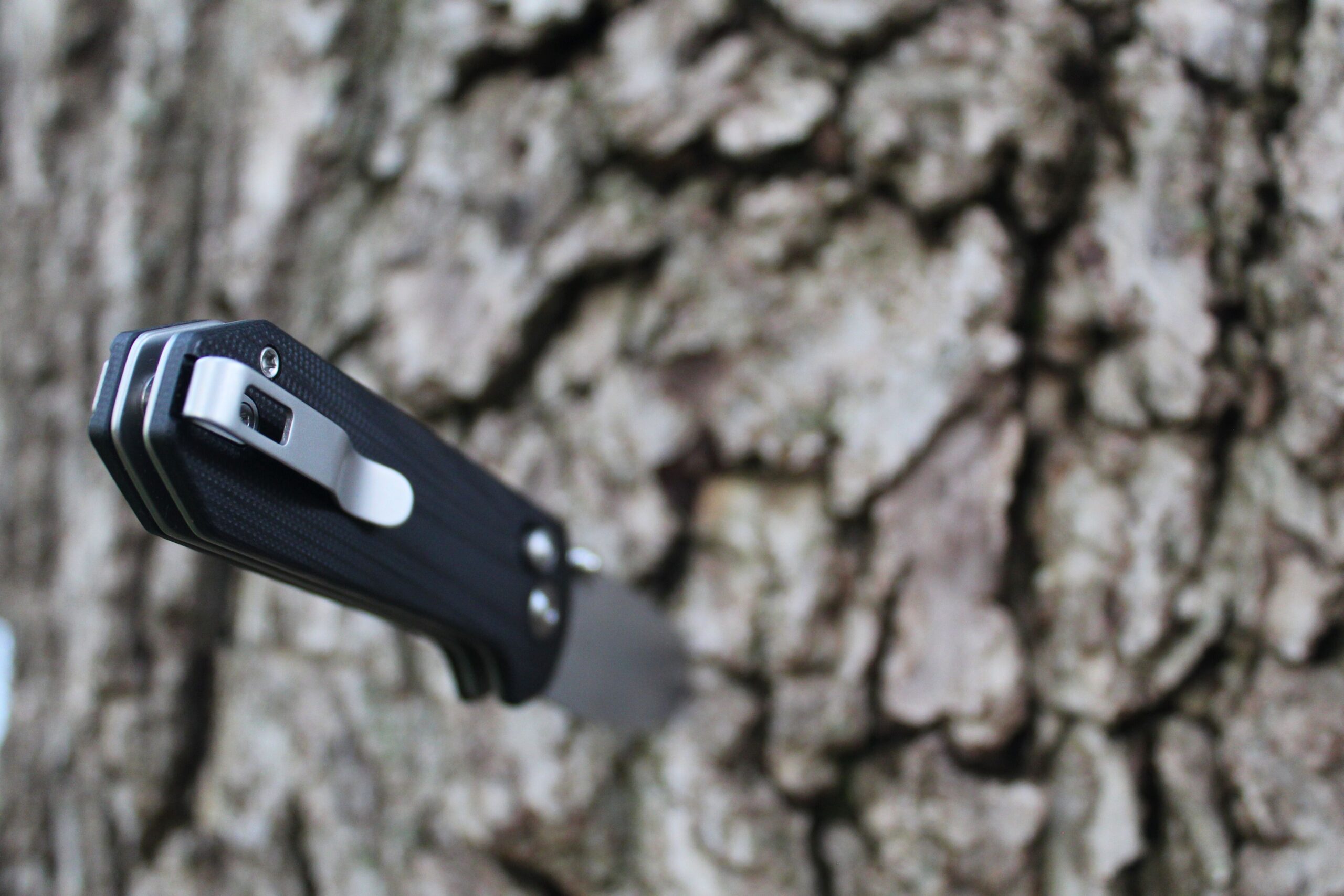 The Civivi Yonder G10 Pocket Knife stabbed into the trunk of a tree with close up of the pocket clip.