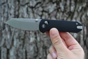 Holding the Civivi Yonder G10 Pocket Knife up while open with a tree as the background