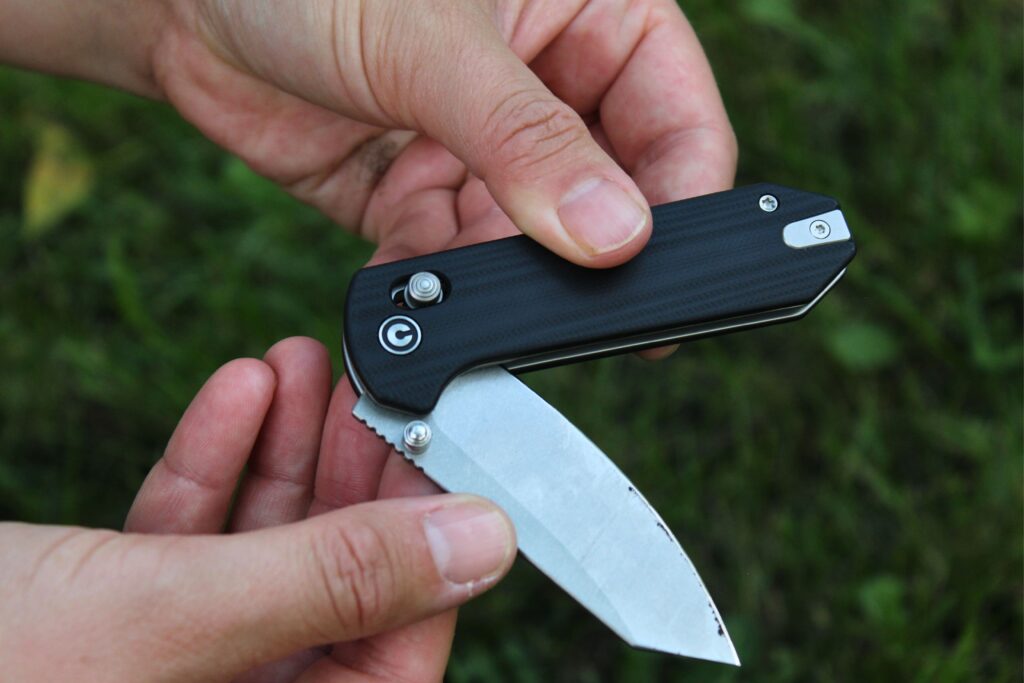 Someone holding the Civivi Yonder G10 Pocket Knife while it is half open with a grassy background