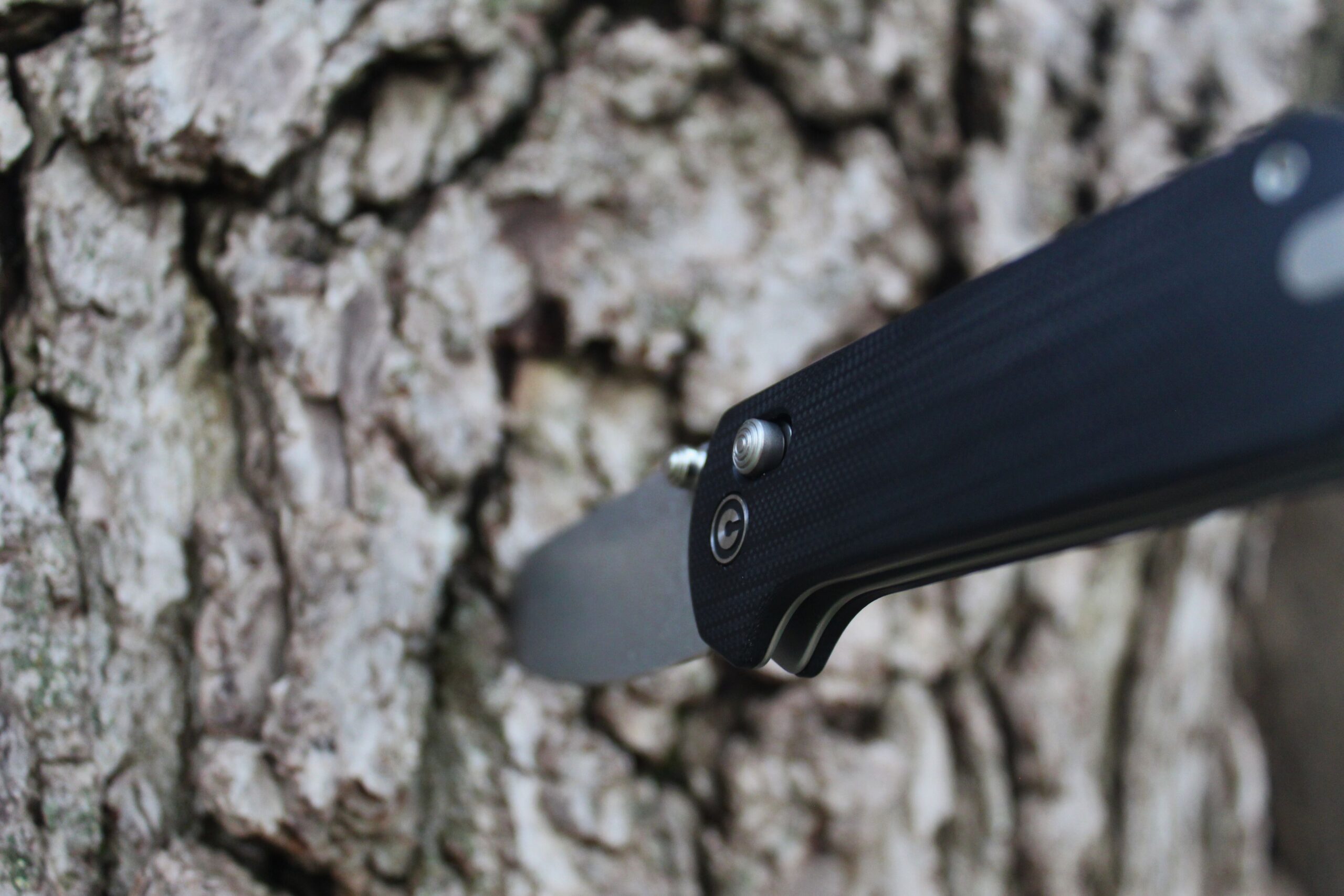 The Civivi Yonder G10 Pocket Knife stabbed into the trunk of a tree with close up of the handle and locking mechanism