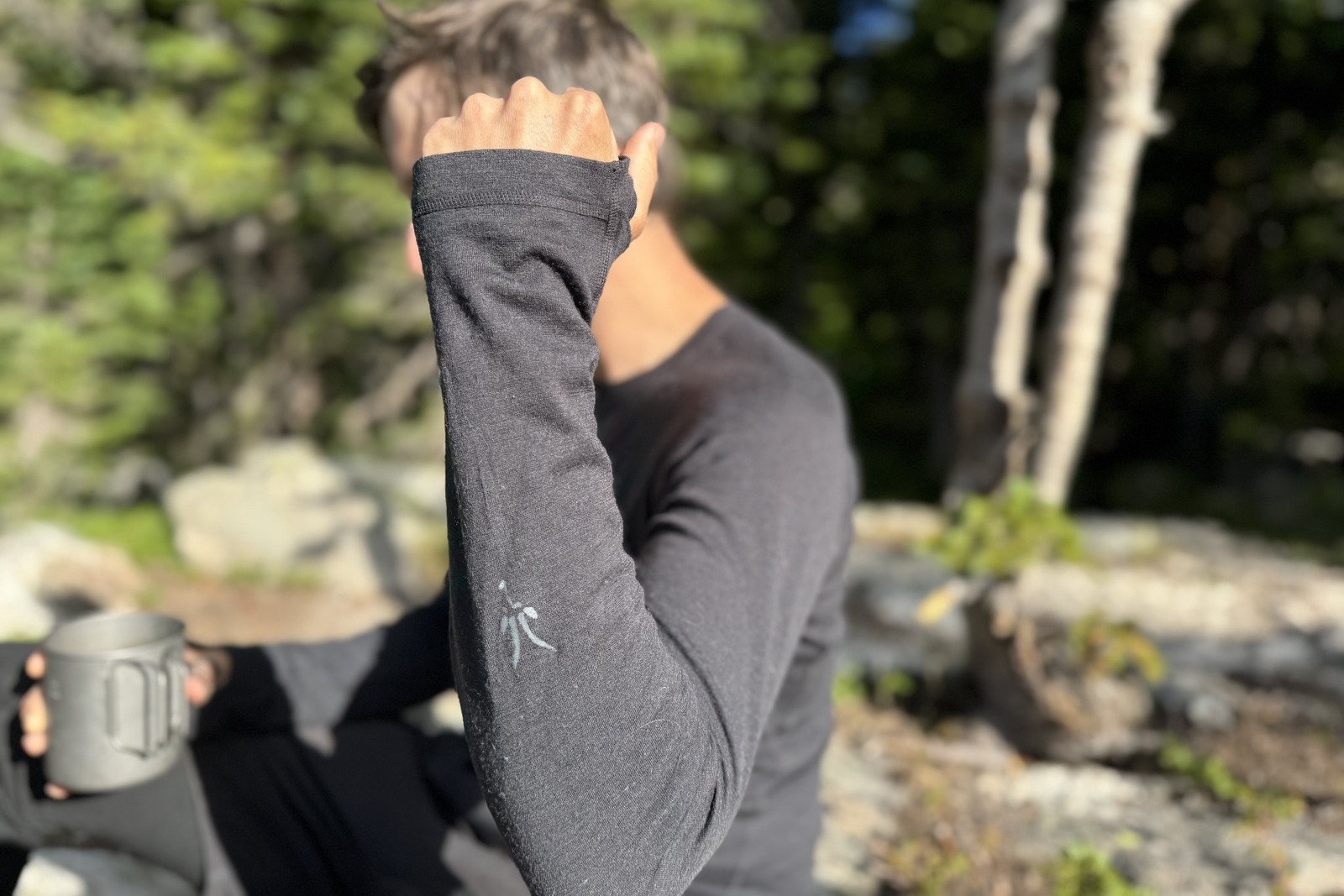 a hiker in a gray base layer raises his forearm to the camera to show the sleeve length