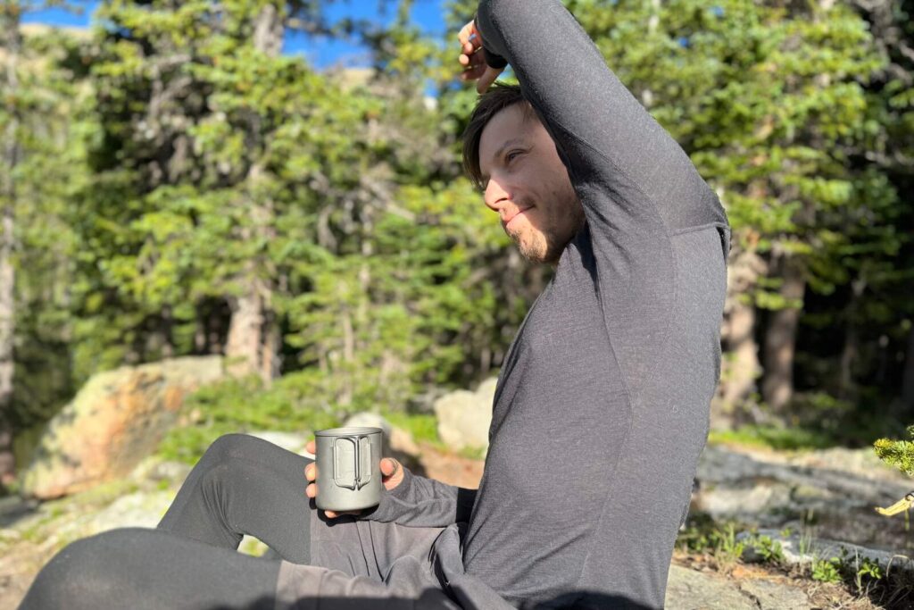 a hiker in a gray base layer raises his arm to show his armpit to the camera