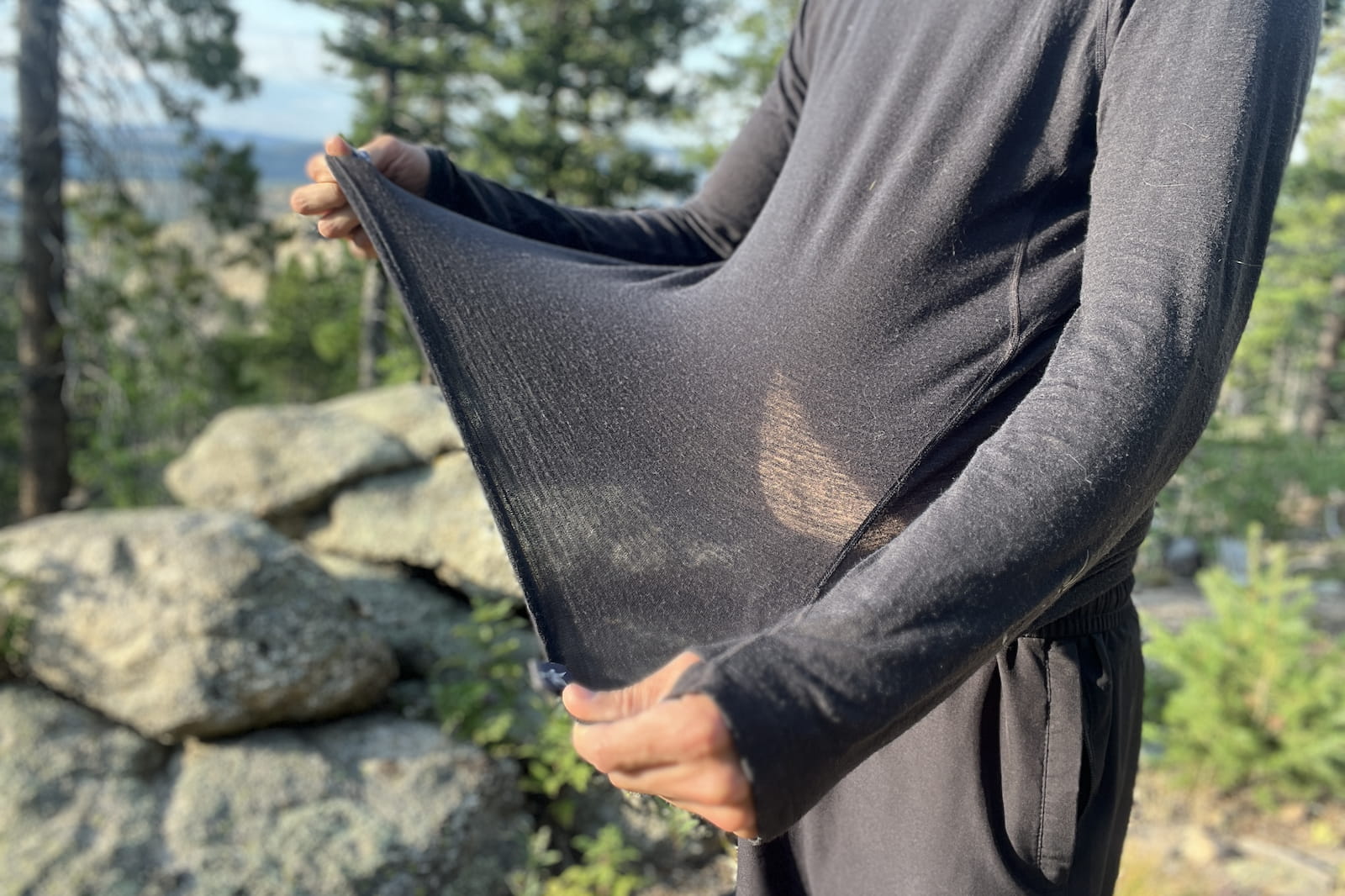 a hiker stretches the fabric of his base layer to show its elasticity and thickness
