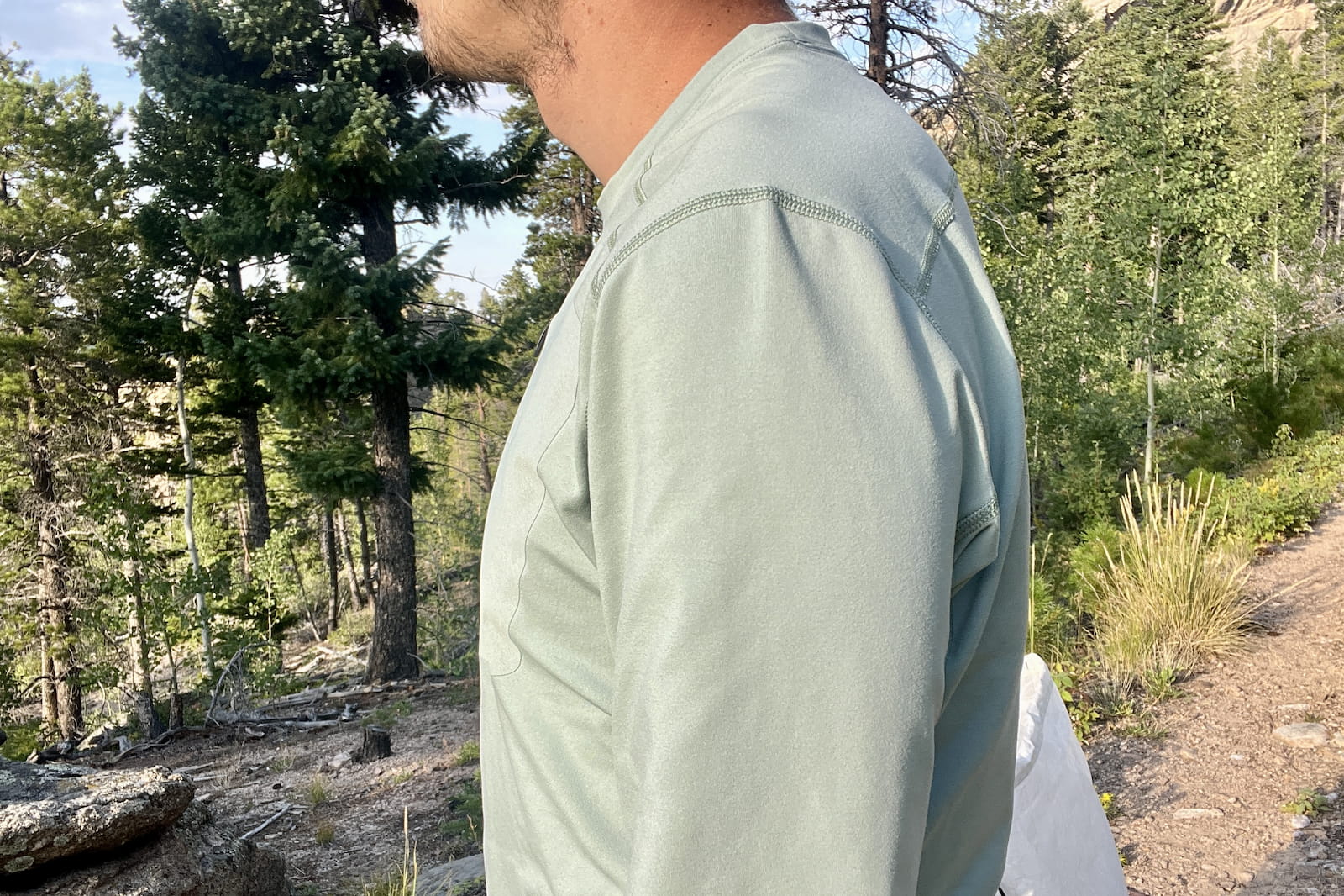 a profile torso shot of a hiker in the woods wearing a light blue base layer.