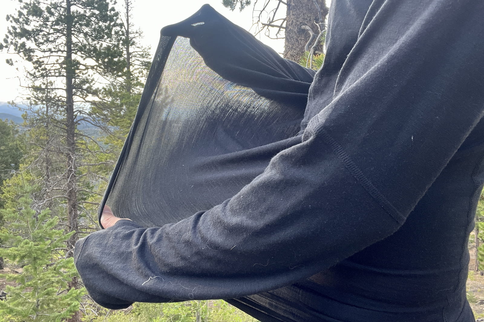 a hiker stretches the fabric of his base layer to show its elasticity and thickness