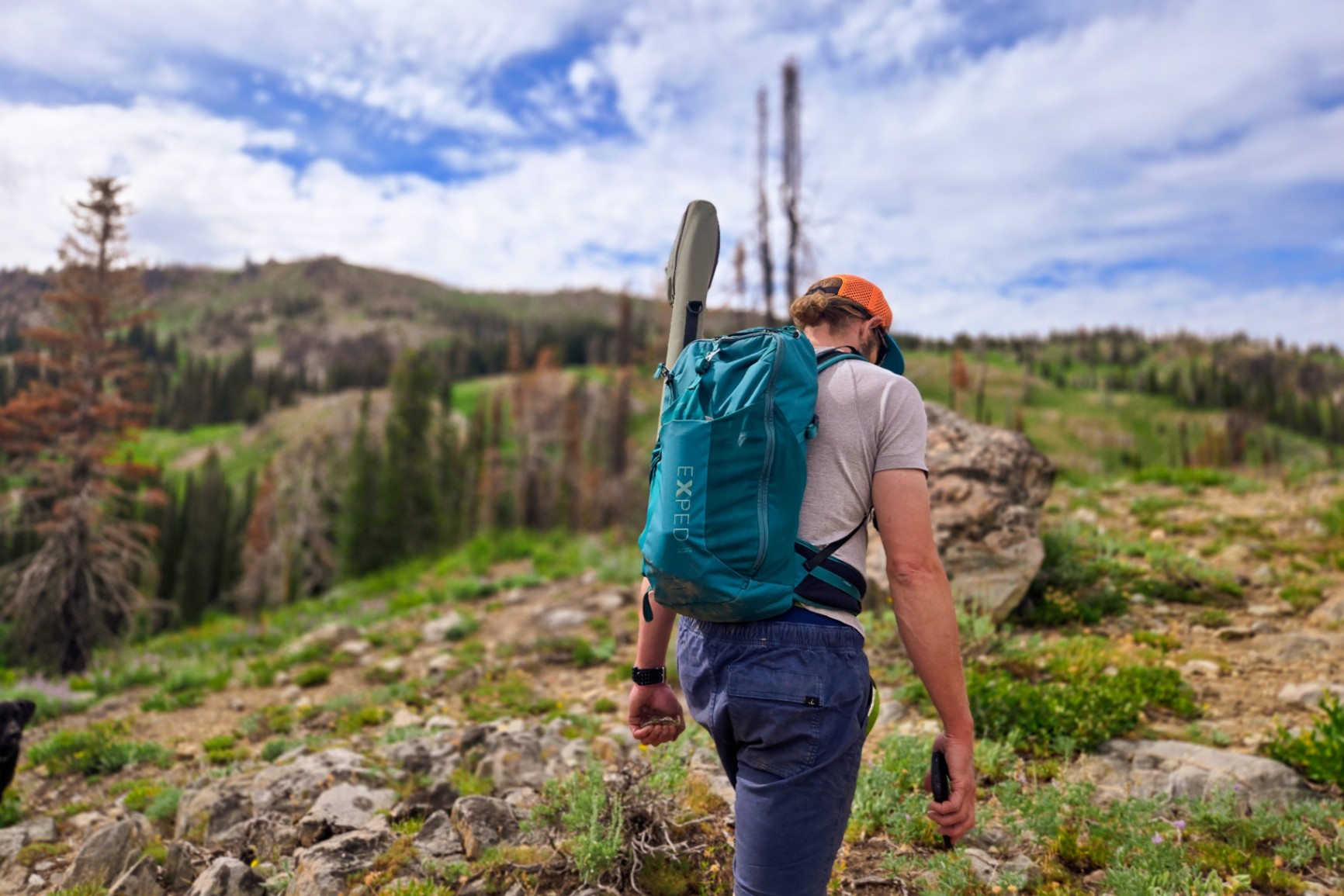 Person with a green EXPED day pack hikes up a rocky trail.