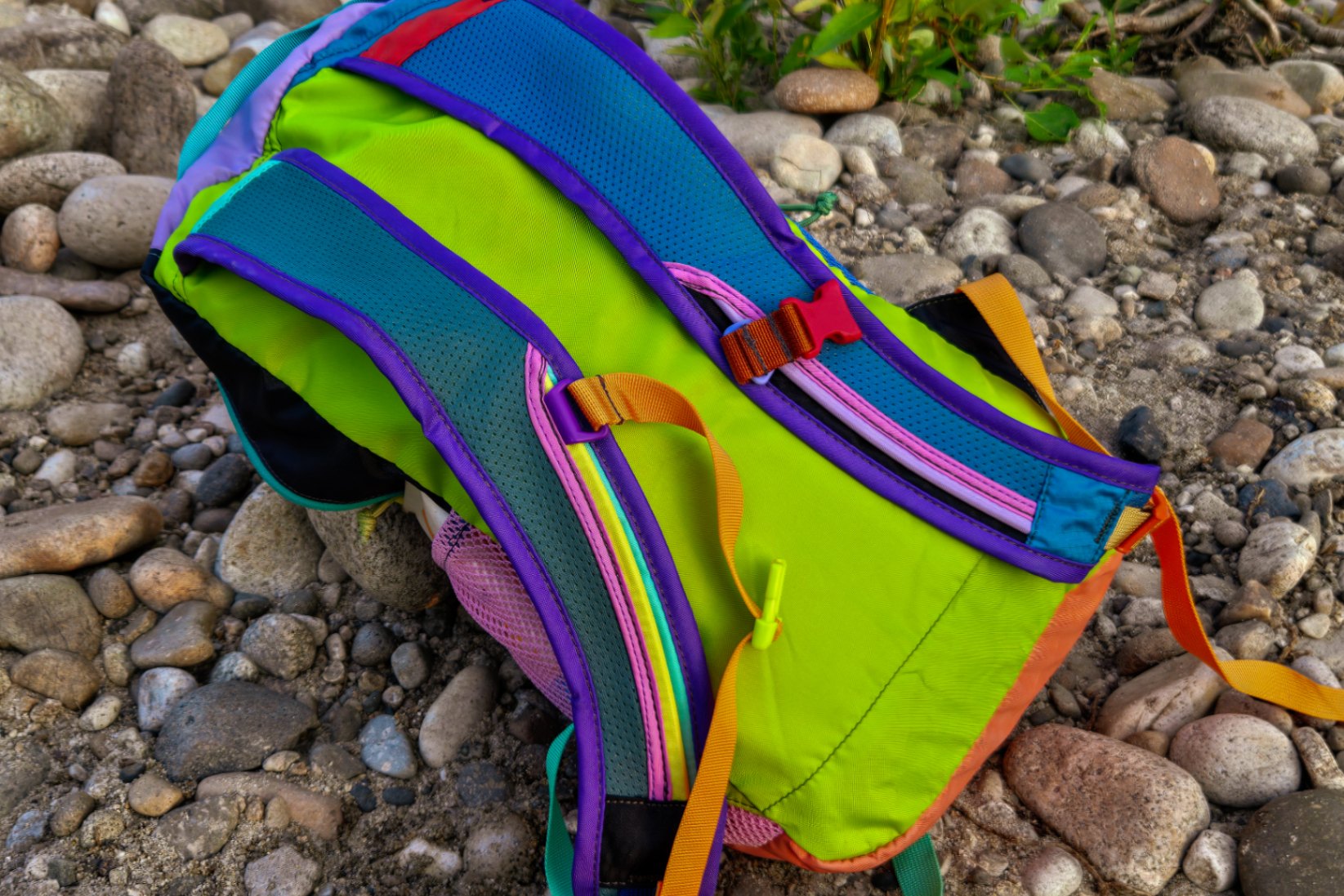 A Cotopaxi daypack lays on the ground. Its lightweight, meshy straps and lack of hipbelt are on display.