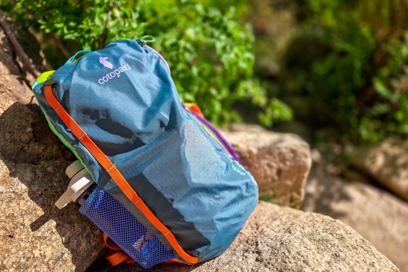 A Cotopaxi Batac 16L pack lays packed up on a rock. Mesh side pockets are on display.