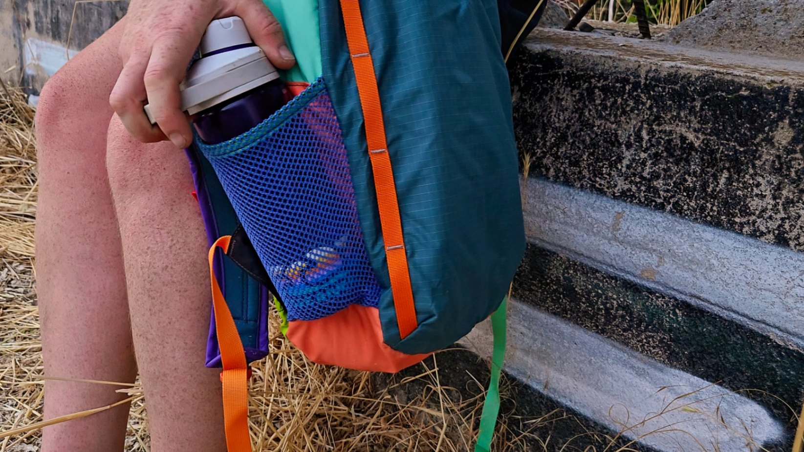 A close up view of a hand pushing a water bottle into the side mesh pocket of the Batac 16.